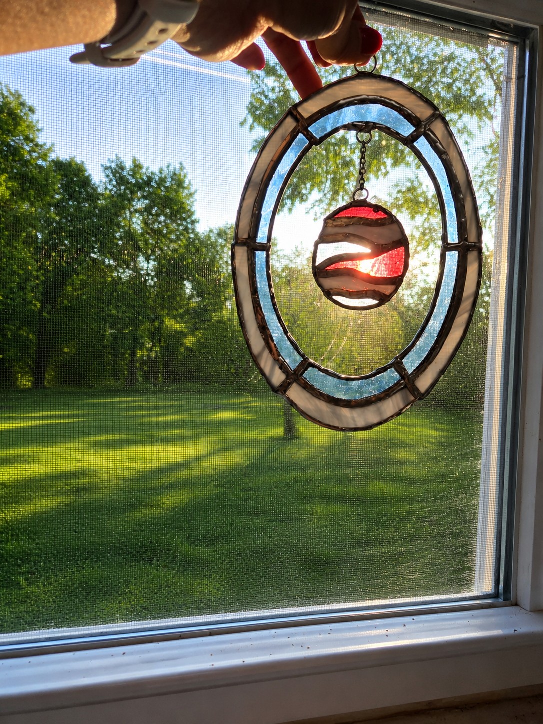 Oval stained glass suncatcher with a hanging red glass moon, held up to a window
